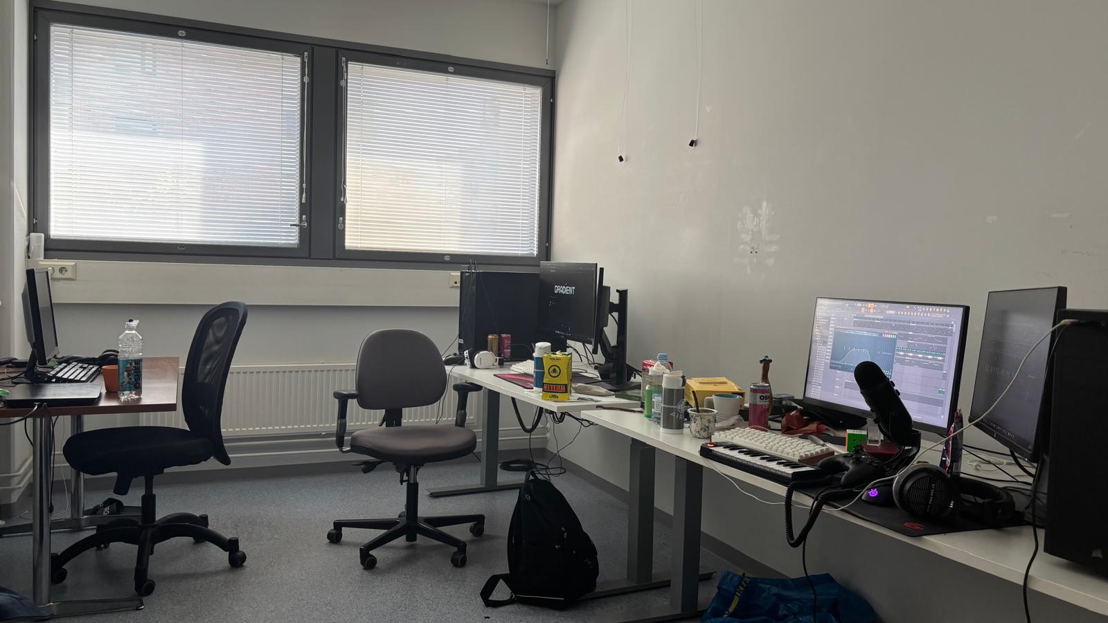 A small game development workspace at night in Turku, with two desks, glowing monitors and a window onto the dark harbour.